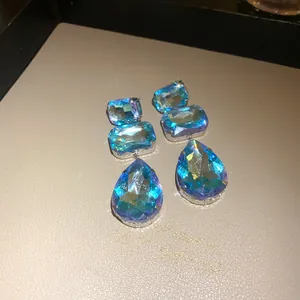 Dettaglio degli orecchini pendenti con cristalli blu a goccia su una base color crema
