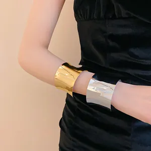 Vista detallada de brazaletes anchos dorados y plateados en el brazo de una modelo