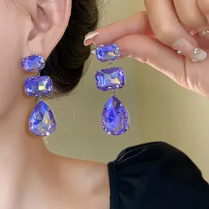 Dettaglio ravvicinato di eleganti orecchini a goccia in cristallo viola sfaccettato.