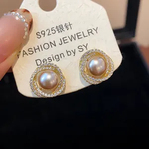 Close-up detail of luxury gold-plated pearl stud earrings with zircon halo on white card