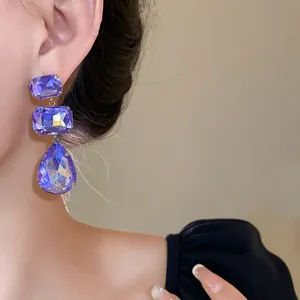 Dettaglio di eleganti orecchini pendenti con cristalli viola quadrati e a goccia