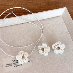 Handmade beaded camellia flower necklace and earrings set on a beige textured tray