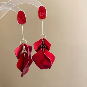 Detailed shot of elegant red acrylic petal drop earrings with gold-tone accents on beige