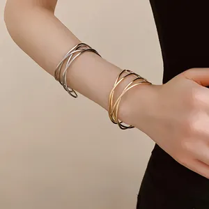 Detailed view of gold and silver multi-layer crossover open bangles on a model's arm