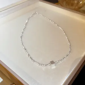 Macro view of a silver faceted bead necklace with a polished minimalist cube pendant