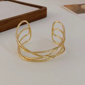Close-up of a minimalist gold multi-layer intertwined open cuff bracelet on white background.