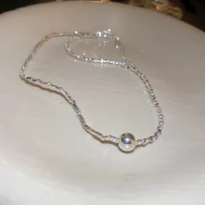 Detailed close-up showing a silver irregular geometric bead necklace with a spherical pendant.