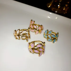 Close-up detail of four gold-plated leaf rings featuring white pink blue and purple enamel