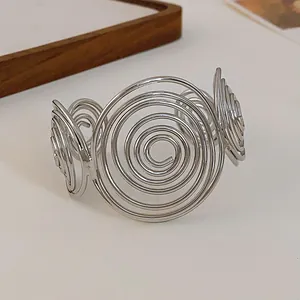 Close-up of minimalist silver-toned cuff bracelet with large spiral metal design