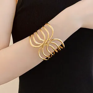 Close-up view of a gold-toned multi-layer crossed open cuff bracelet on a wrist