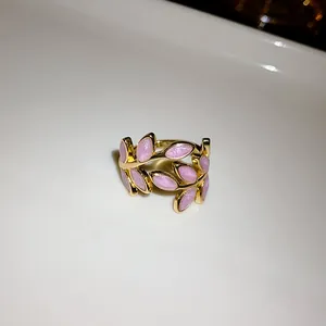 Close-up view of a gold-plated leaf open ring with glittering pink enamel finish details.
