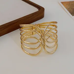 Macro detail of a gold multi-layer crossover open cuff bracelet with spring hinge mechanism