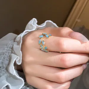 Close-up of elegant gold leaf open ring with light blue stones on model's finger