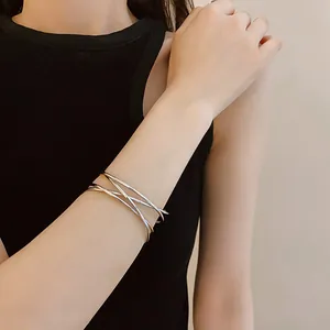Close-up view of minimalist silver multi-layer crisscross open bangle bracelet on wrist