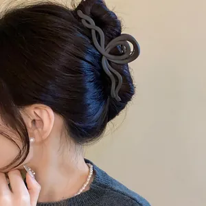 Close-up of a matte black wave-twisted shark clip styled in a classic hair bun.
