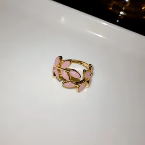 Detailed view of a gold-tone open ring with pink enamel leaf patterns on white base