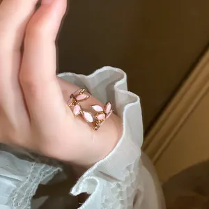 Macro view of adjustable gold-tone leaf ring with pink enamel accents on hand