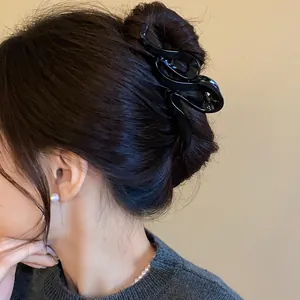 Detail of wave-shaped black acrylic hair claw clip used in an elegant bun hairstyle