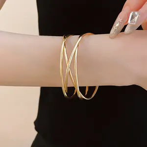 Elegant gold-tone multi-layer crisscross open bangle bracelet worn on wrist for a minimalist look