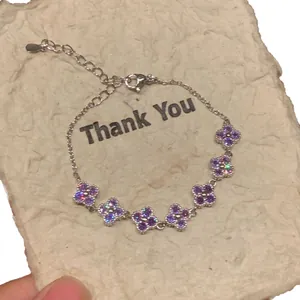 Elegante zilverkleurige armband met paarse zirkonia bloemhangers op getextureerd papier