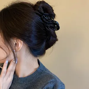 Close-up detail of a minimalist black wavy acrylic hair claw clip used in a bun hairstyle.