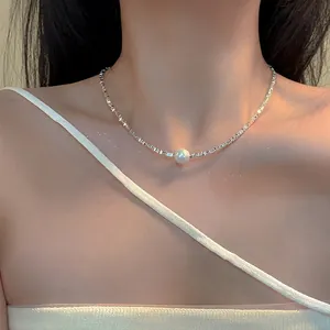 Close-up view of a silver irregular metal necklace with a central white pearl on a model.
