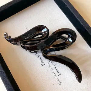 Detailed view of a glossy black acrylic hair claw clip with a stylish wavy design.