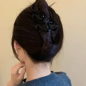 Close-up view of a wavy black acrylic hair claw clip used in a stylish bun hairstyle.