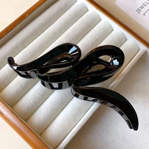 Close-up view of a minimalist glossy black wavy acrylic hair claw clip in a display box