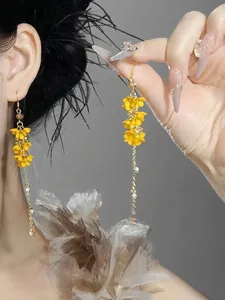 Primo piano di orecchini pendenti con fiori gialli stile foresta con perle e nappe oro