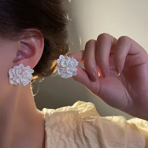 Detail of white floral stud earrings worn on ear and held to show delicate petals