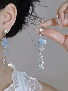 Dettaglio di orecchini pendenti lunghi con pietre azzurre e bottoni di cristallo
