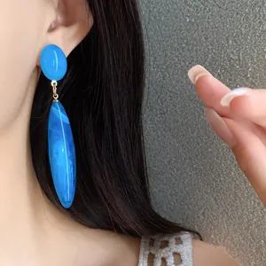 Primer plano de un pendiente de gota de acrílico azul veteado sobre la oreja