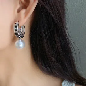 Elegant metallic hoop earring with pearl pendant and cross orb design worn by a model