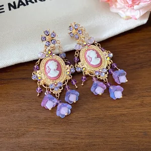 Vintage cameo earrings with purple rhinestones and tassel flowers on a wooden background.