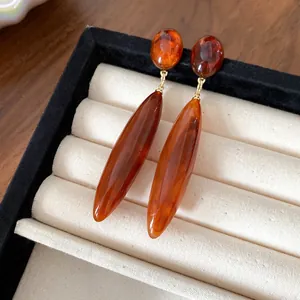 Primer plano de pendientes de gota de acrílico ámbar en bandeja de joyas beige.