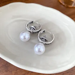 Detailed shot of retro gothic silver hoop earrings with white pearl drop and cross orb charm