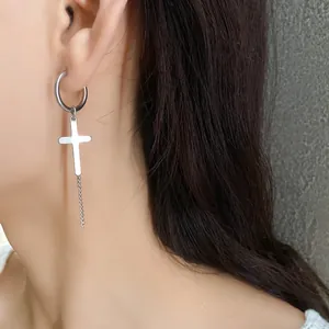 Detailed view of a silver-tone cross earring worn on an ear, featuring a hoop and chain.