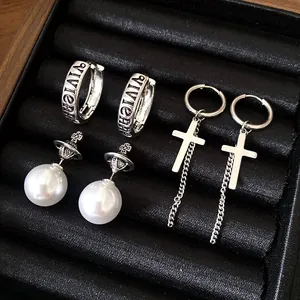 Detail of silver-tone cross earrings and pearl studs with orb design on black velvet tray.