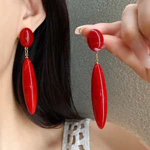 Vista detallada de pendientes de gota de acrílico rojo brillante con patrón jaspeado.