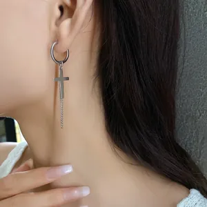 Close-up detail of a silver cross dangle earring with chain worn by a model for fashion