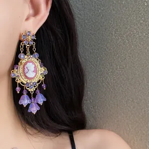 Close-up of elegant vintage cameo earrings with purple flower tassels and crystals
