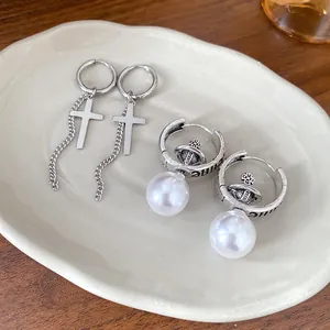 Detailed close-up of silver-tone cross chain and elegant pearl orb dangle hoop earrings.