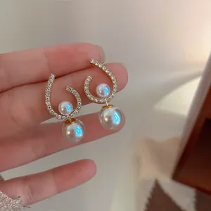 Close-up detail of elegant gold-plated earrings with white pearls and sparkling rhinestones