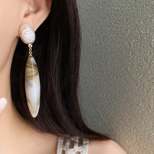 Vista detallada de pendientes largos de acrílico jaspeado usados por una modelo real