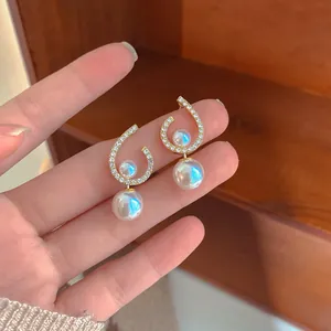 Detail of elegant twisted rhinestone earrings with iridescent pearls held by hand.