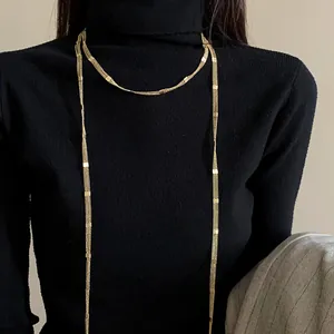 Detailed close-up of a long minimalist gold chain necklace worn over a black turtleneck.