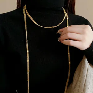 Detailed view of a long gold chain sweater necklace on a black turtleneck.