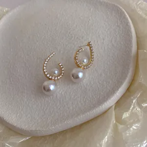 Close-up detail of twisted micro-paved stud earrings with elegant dangling white pearls