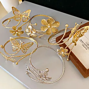 Macro view of several gold and silver open bracelets with flower and butterfly motifs.